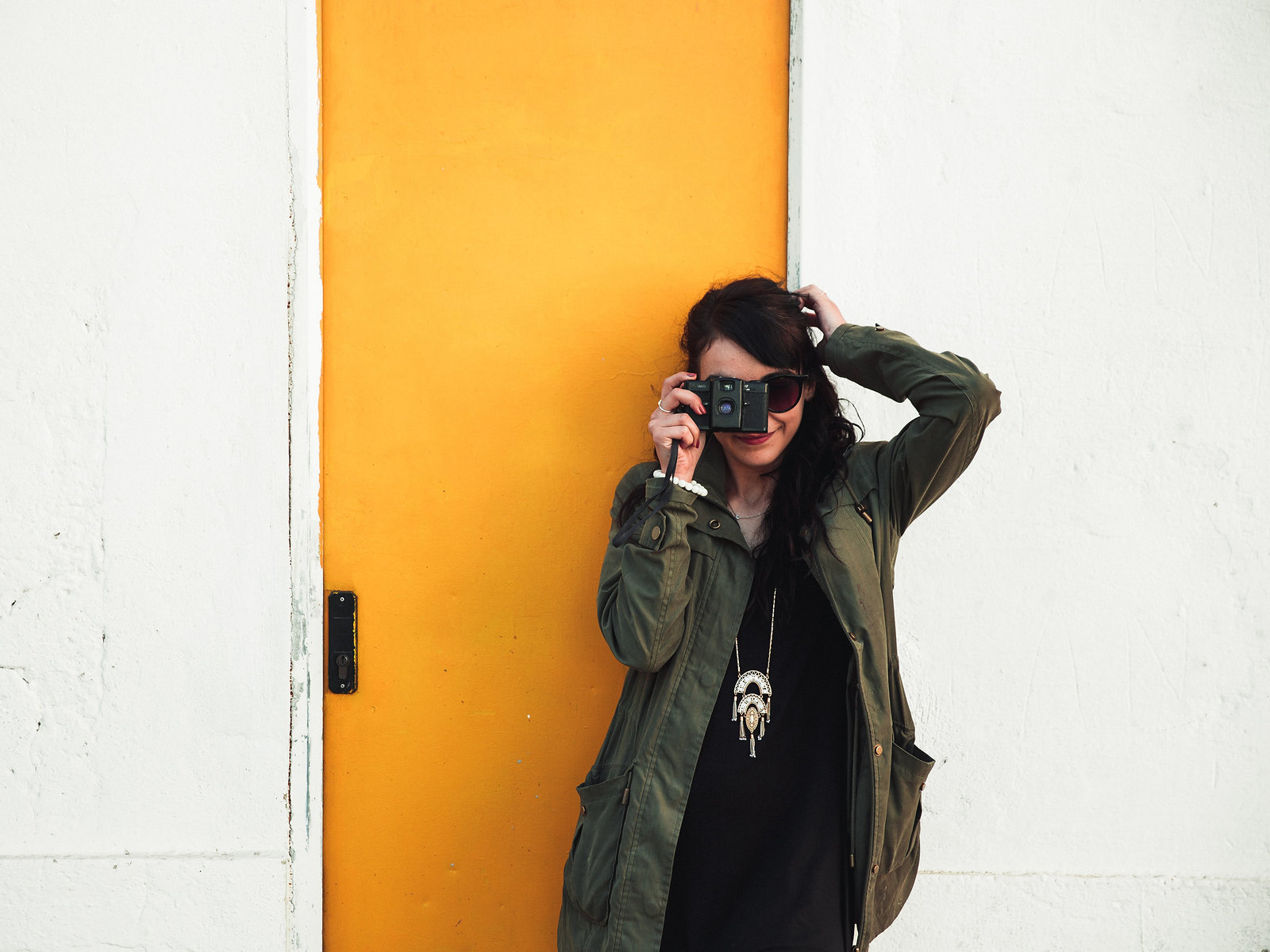 A photographer with a film camera against a bright yellow door