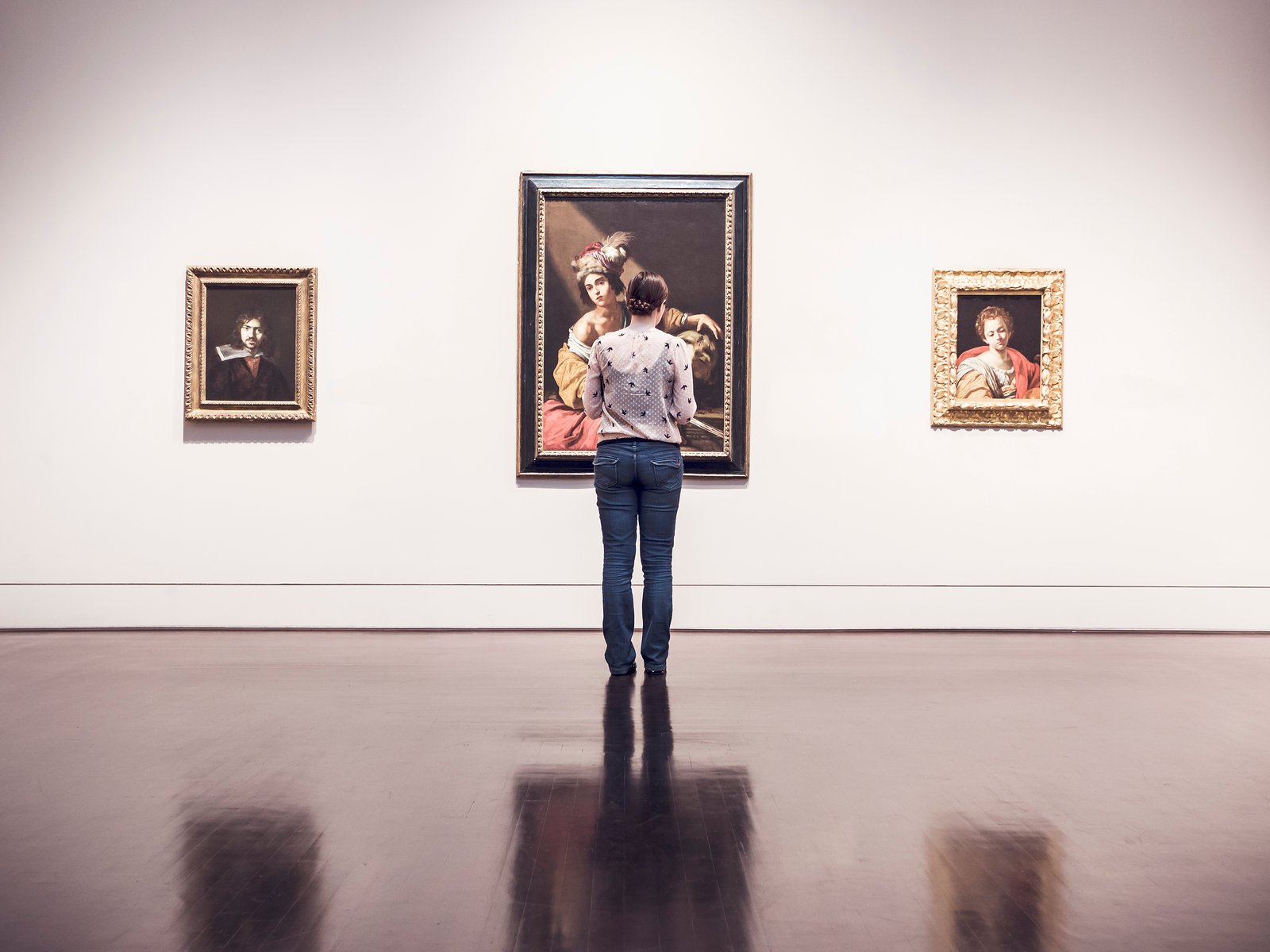 A visitor looking at framed paintings in a bright white gallery