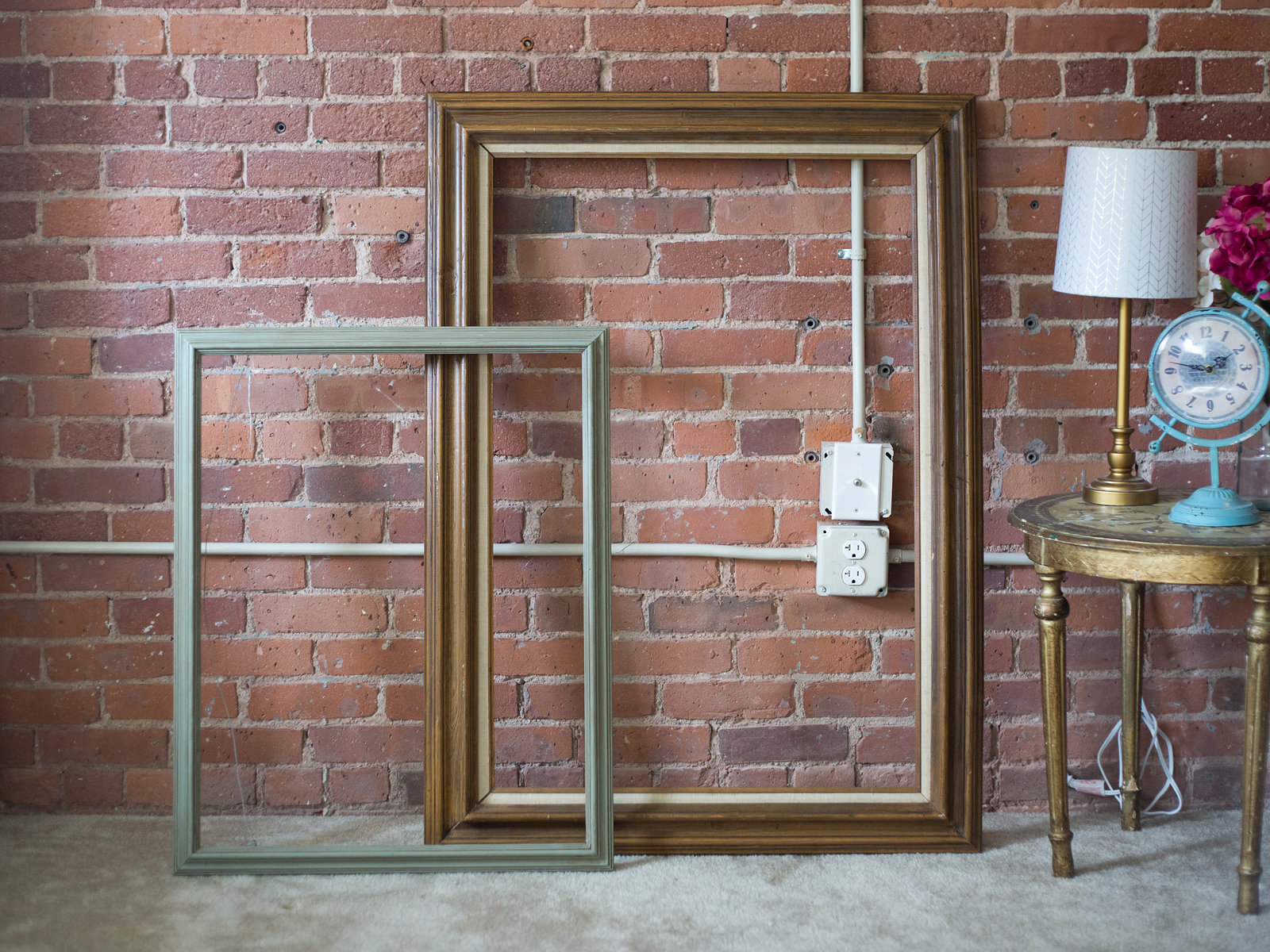 Two empty wooden picture frames, one pale green and one walnut, leaning against a brick wall